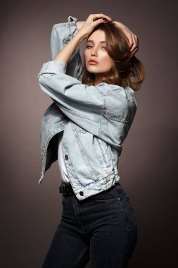Uzun akan saçlı güzel esmer kız Kot ceket ve kot pozlar başında stüdyoda koyu arka plan üzerinde ellerini tutarak giyinmiş