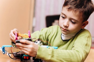 Çalışkan çocuk yeşil Kazak giymiş masa başında bilgisayarla oturur ve robot Robotik okul robot Oluşturucu yapar