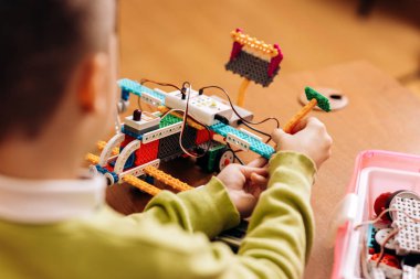 Sedulous çocuk yeşil Kazak giymiş Robotik okuldaki masada oturur ve bir robot Robotik Oluşturucu yapar