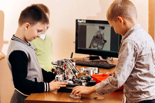 Three smart boys are making robots from the robotic constructor at the desk with computer in the School of Robotics — Stock Photo, Image