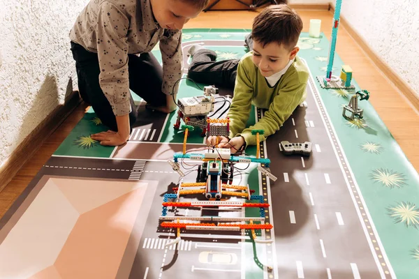 Dos chicos juegan con robots que crearon del constructor robótico en la colorida pancarta en el suelo de la Escuela de Robótica — Foto de Stock