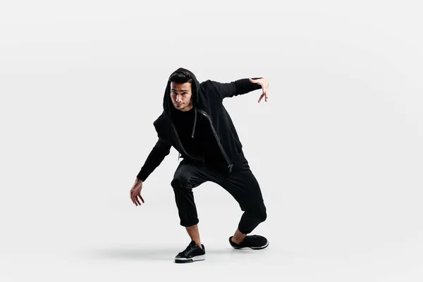Mörkhårig snygg ung man klädd i en svart tröja och svarta byxor gör stiliserade rörelser av gatan danser — Stockfoto
