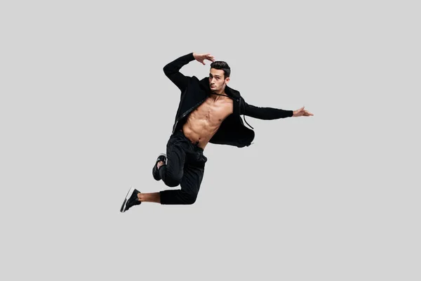 Bonito jovem dançarino de rua dançando vestido com calças pretas e uma camisola em um tronco nu pula em um fundo branco — Fotografia de Stock
