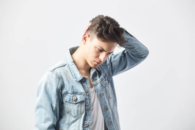 Beyaz bir t-shirt ve kot ceket giymiş düşünceli esmer adam baş beyaz arka planda stüdyoda elini tutar