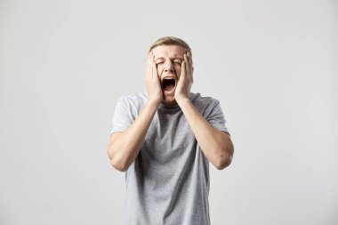 Üzgün adam beyaz bir t-shirt giymiş onun ellerini onun yanaklarda tutar ve stüdyoda beyaz zemin üzerine Not