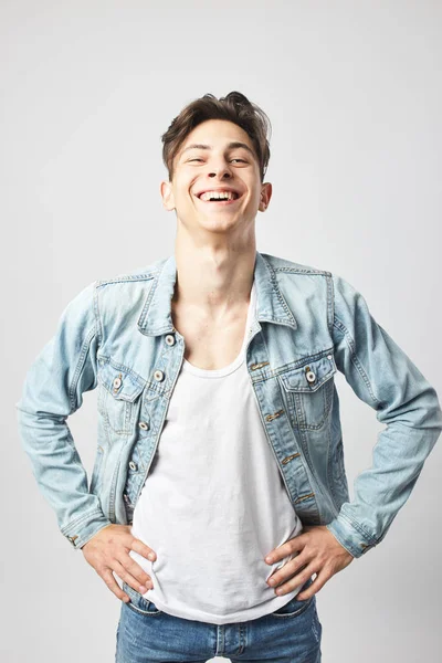 Cara rindo cara de cabelos escuros vestido com uma camiseta branca e uma jaqueta de ganga fica no fundo branco no estúdio — Fotografia de Stock