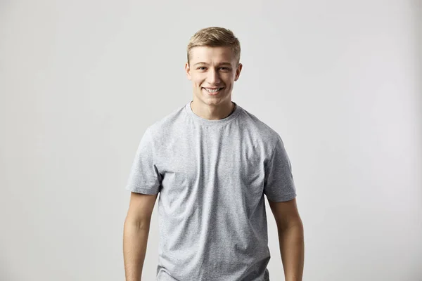 Sorrindo cara vestido com uma camiseta branca fica no fundo branco no estúdio — Fotografia de Stock