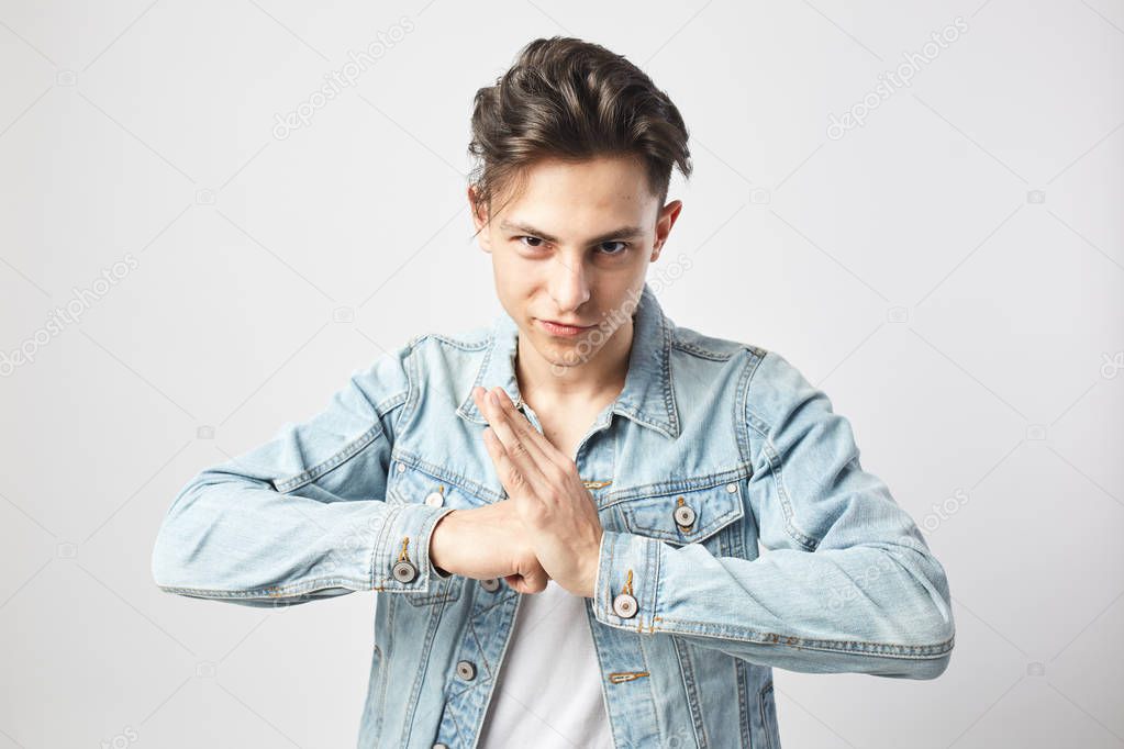 Young dark-haired guy dressed in a white t-shirt and a denim jacket ready to fight on the white background in the studio