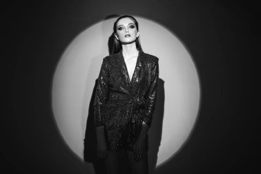 Siyah beyaz portre saç geri çekti ve bir parlayan elbise kapının g parlak spot duvarda yanında şık makyaj ile trendy kız