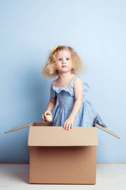 Açık mavi elbiseli, sarı çiçek saç ve onun el tribünlerde arka planda karton kutu mavi duvar boyalı yumurta ile sevimli küçük kız.