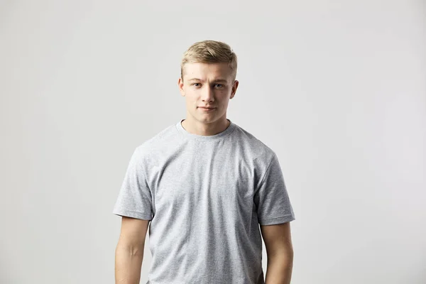 Blond kille klädd i en vit t-shirt står på den vita bakgrunden i studion — Stockfoto