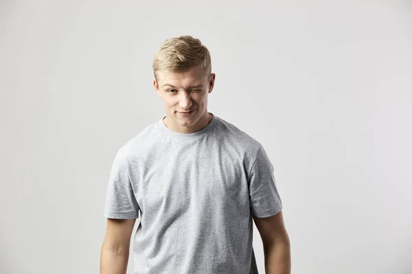 Winking blond kille klädd i en vit t-shirt står på den vita bakgrunden i studion — Stockfoto