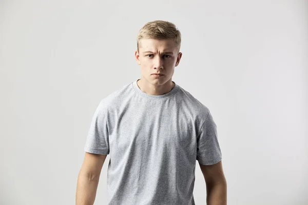 Seriózní blond člověk oblečený v bílé tričko stojí na bílém pozadí v ateliéru — Stock fotografie