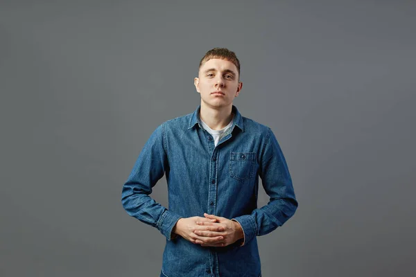 Cara vestida com uma camiseta branca, jeans e jeans de pé com os braços dobrados no estúdio no fundo cinza — Fotografia de Stock