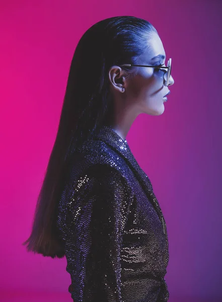 Modemädchen mit langen Haaren und runder Sonnenbrille in schwarzem Kleid posiert im Atelier im Neonlicht — Stockfoto