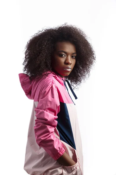 Young curly brown-haired girl dressed in the pink sport jacket stands at the white background in the studio — Stock Photo, Image