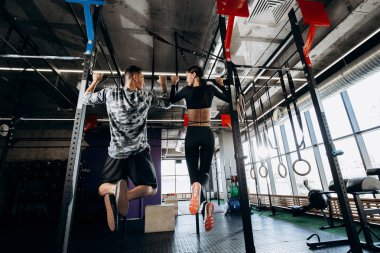 İnce kız ve atletik erkek spor kıyafetlerini giymiş salonunda çubuğunda yukarı çekerek