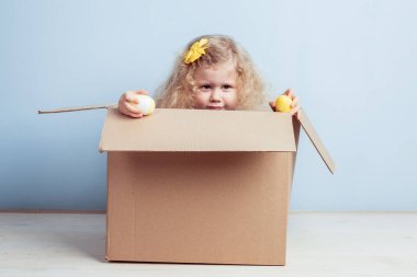 Sevimli küçük kız onun saç ve elleri boyalı yumurta Sarı çiçekli karton kutu mavi duvar arka planda oturur.