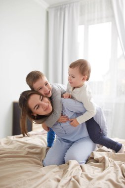 Güzel genç anne ve pijama giymiş iki küçük oğulları hafif rahat yatak odasında yatağın üstüne iyi eğlenceler