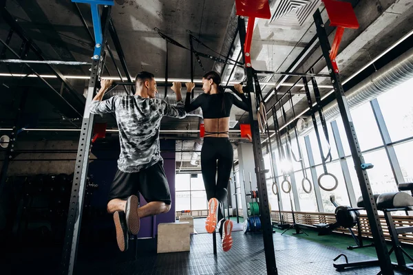 Szczupła dziewczyna i lekkoatletycznego mężczyzna ubrany w odzież są ciągnąc się na pasku w siłowni — Zdjęcie stockowe