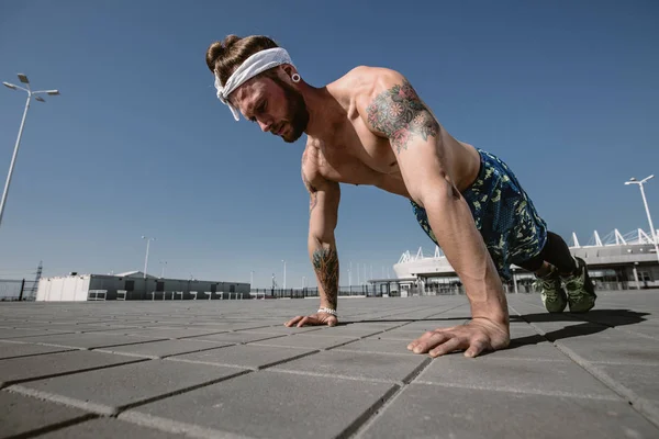 Esportista sem camisa bonito olhando para longe fazendo push up exercício no chão de treino ao ar livre no dia ensolarado brilhante. Estilo de vida desportivo — Fotografia de Stock