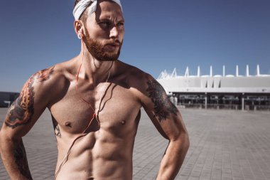 Açık havada egzersiz zeminde eğitimden sonra rahatlatıcı. Yakışıklı gömleksiz sporcu uzakta müzik kentsel poz dinleme earphones ile parlak güneşli bir günde açık arıyor. Spor yaşam tarzı