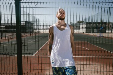 Atletik beyaz kafa bandı adamla beyaz t-shirt, siyah tayt giymiş ve güneşli bir günde Bahçesi çit yaslanmış duran mavi şort