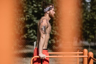 Kafa bandı ile çıplak gövde siyah tayt ve güneşli bir günde amuda asimetrik paralel dışında spor zemin üzerinde kırmızı şort giymiş genç atletik adam