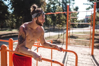 Siyah tayt ve güneşli bir spor zemin dışında asimetrik paralel yanındaki kırmızı şort standları atletik çıplak gövde ile kafa bandı erkekte giymiş