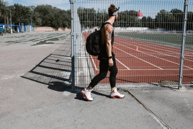 Kafa bandı atletik adam siyah spor elbise sırt çantası ile onun omuzlarında Bahçesi çit boyunca güneşli bir günde giymiş