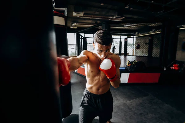 Kum torbası içinde jimnastik salonu boks halka arka plan üzerinde kırmızı boks eldiven çıplak bir gövde ile sporcu hits — Stok fotoğraf
