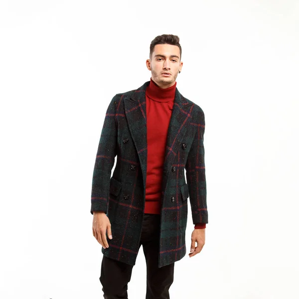 Jeune homme élégant vêtu de col roulé rouge, pantalon brun et un manteau à carreaux se tient sur le fond blanc — Photo