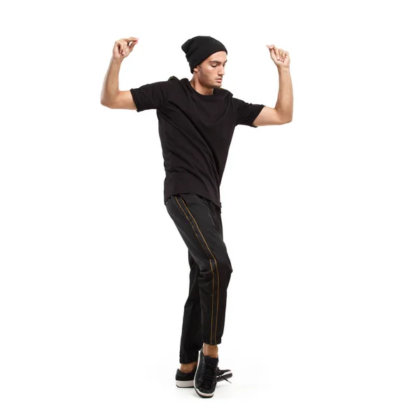 Jeune homme élégant vêtu de t-shirt noir, pantalon à rayures sur les côtés et chapeau noir danse sur le fond blanc dans le studio — Photo