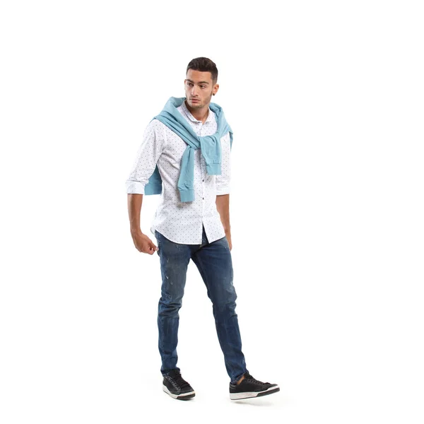 Jeune homme élégant vêtu d'une chemise blanche et d'un pull bleu drapé sur ses épaules et de jeans pose sur le fond blanc — Photo