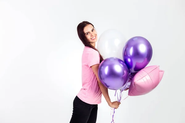 Chica feliz vestida con camiseta rosa y jeans sostiene globos en sus manos sobre el fondo blanco en el estudio — Foto de Stock