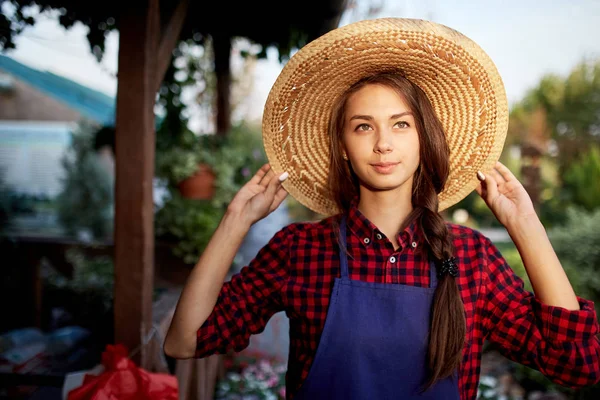 在一个阳光明媚的日子里, 戴着草帽的迷人女孩园丁站在美丽的花园里. — 图库照片