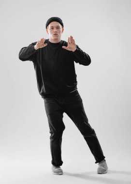 Adam dansçı giymiş siyah kot, tişört, şapka ve gri spor ayakkabı beyaz arka plan üzerinde stüdyoda dans ediyor