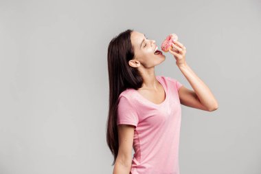 Güzel kız pembe gömlek giymiş pembe ağız sulandıran çörek beyaz arka plan üzerinde çalışacak