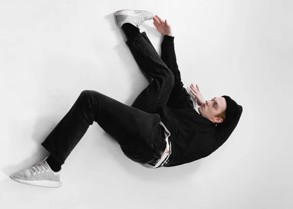 Taneční Freestyle tanečník, oblečená v černé džíny, triko, klobouk a šedé tenisky leží na podlaze v ateliéru na bílém pozadí — Stock fotografie