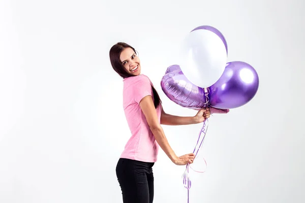 Chica feliz vestida con camiseta rosa y jeans sostiene globos en sus manos sobre el fondo blanco en el estudio — Foto de Stock