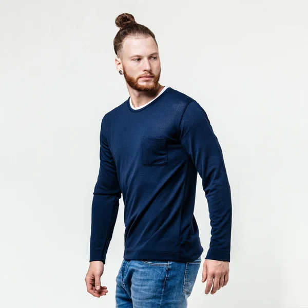 Homme élégant avec coiffure barbe et chignon vêtu d'un pull à manches longues bleu et un jean pose en studio sur le fond blanc — Photo