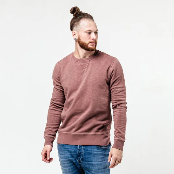 Homme à la mode avec coiffure barbe et chignon vêtu d'un pull à manches longues brun clair et un jean pose en studio sur le fond blanc — Photo