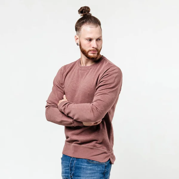 Homme à la mode avec coiffure barbe et chignon vêtu d'un pull à manches longues brun clair et un jean pose en studio sur le fond blanc — Photo