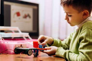 Yeşil Kazak giymiş çocuk bilgisayar ve robot Oluşturucu ile masada oturur ve bir robot yapar
