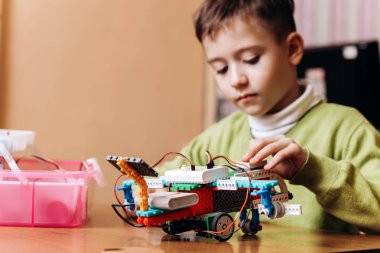 Yeşil Kazak giymiş çocuk masa başında bilgisayarla oturur ve o robot kurucu Robotik okul içinde yapılan robot bakar