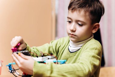 Çalışkan çocuk yeşil Kazak giymiş masa başında bilgisayarla oturur ve robot Robotik okul robot Oluşturucu yapar