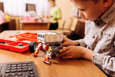 Sedulous çocuk gri gömlek giymiş bir robot Robotik okul masasında robot Oluşturucu yapar