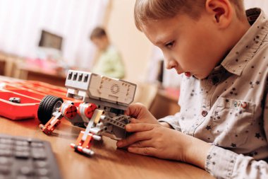 Sedulous çocuk gri gömlek giymiş bir robot Robotik okul masasında robot Oluşturucu yapar