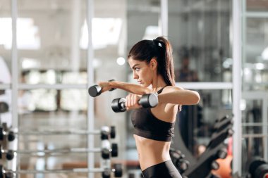 Kas spor salonunda dumbbells ile siyah spor top ve tayt giymiş güzel atletik kız kurar