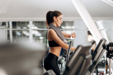 Spor salonunda bir koşu bandı üzerinde siyah spor top ve havlu boynunda tayt giymiş esmer atletik kız inşaat dışarı